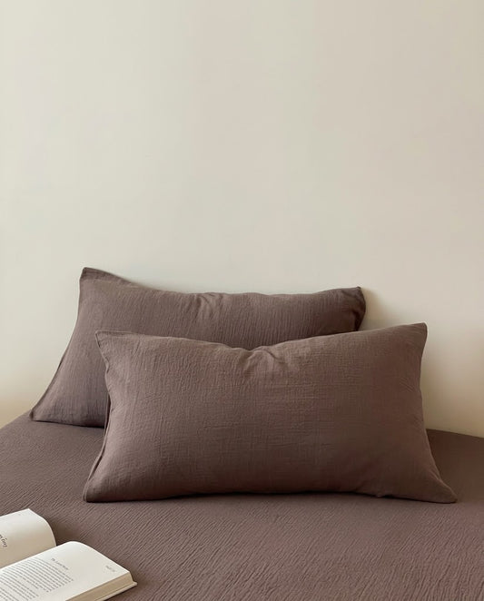 Two Espresso muslin cotton double gauze pillowcases on a matching sheet with an open book