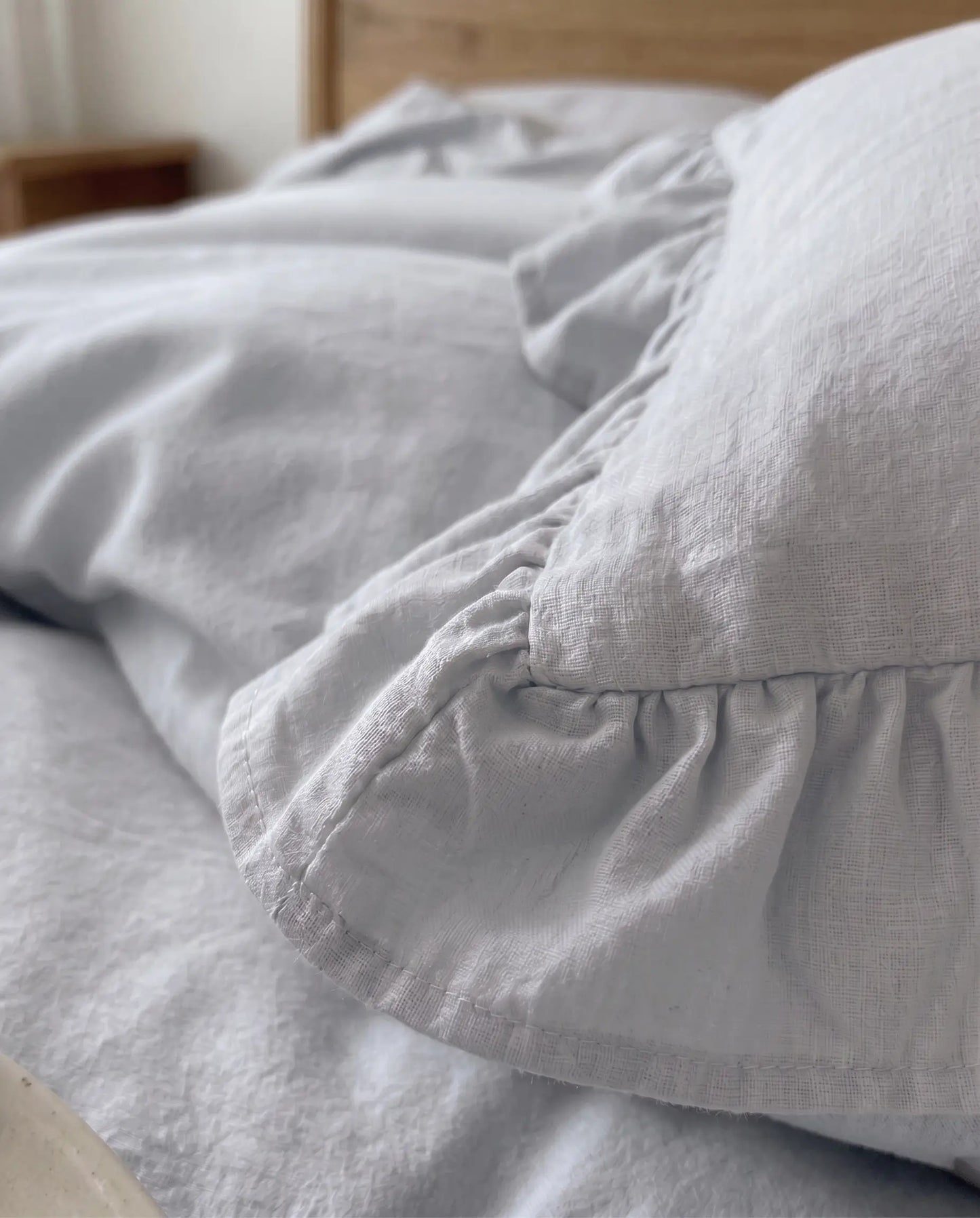 Close-up of mist blue ruffle pillow sham featuring soft textured cotton fabric and romantic gathered trim detailing