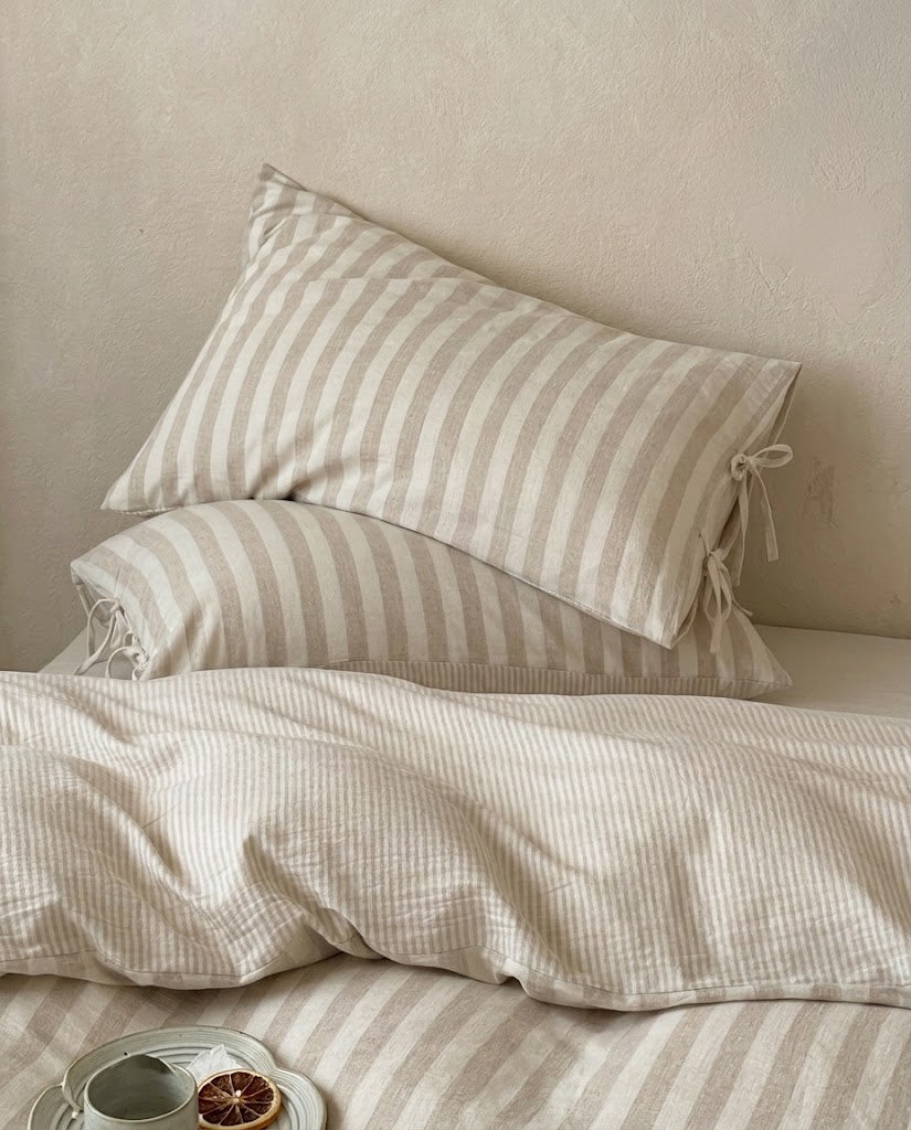 Oatmeal striped cotton linen pillowcases with bow tie closures stacked on a pinstripe duvet cover