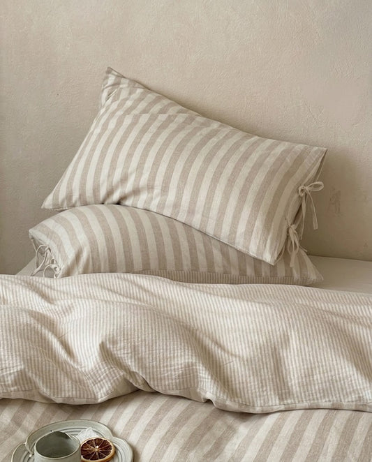 Oatmeal striped cotton linen pillowcases with bow tie closures stacked on a pinstripe duvet cover