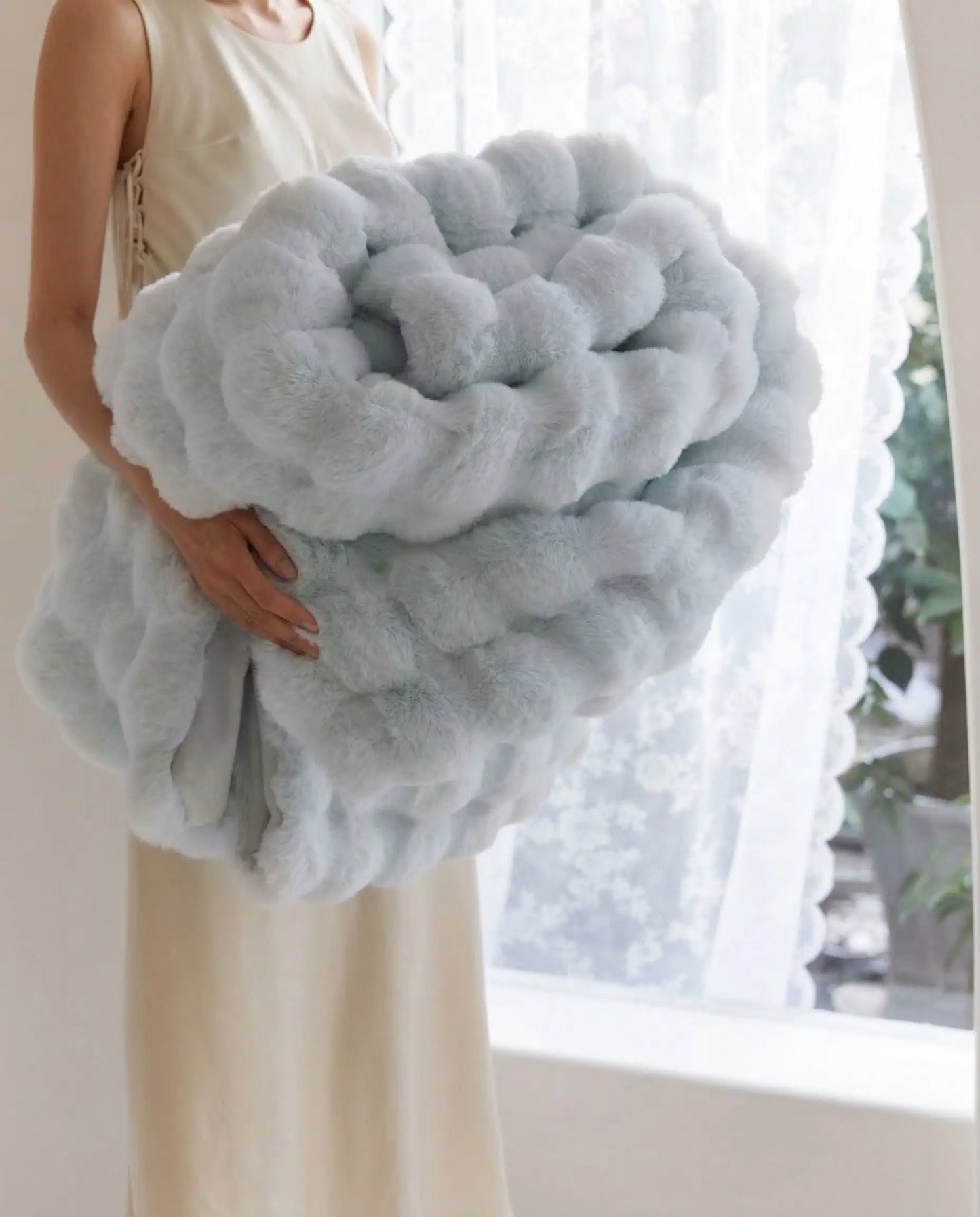 Person holding folded DORMÉ Studio Marshmallow Ultra Plush Blanket in soft blue color showing thick cloud like plush texture.