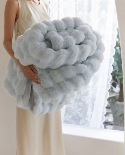 Person holding folded DORMÉ Studio Marshmallow Ultra Plush Blanket in soft blue color showing thick cloud like plush texture.
