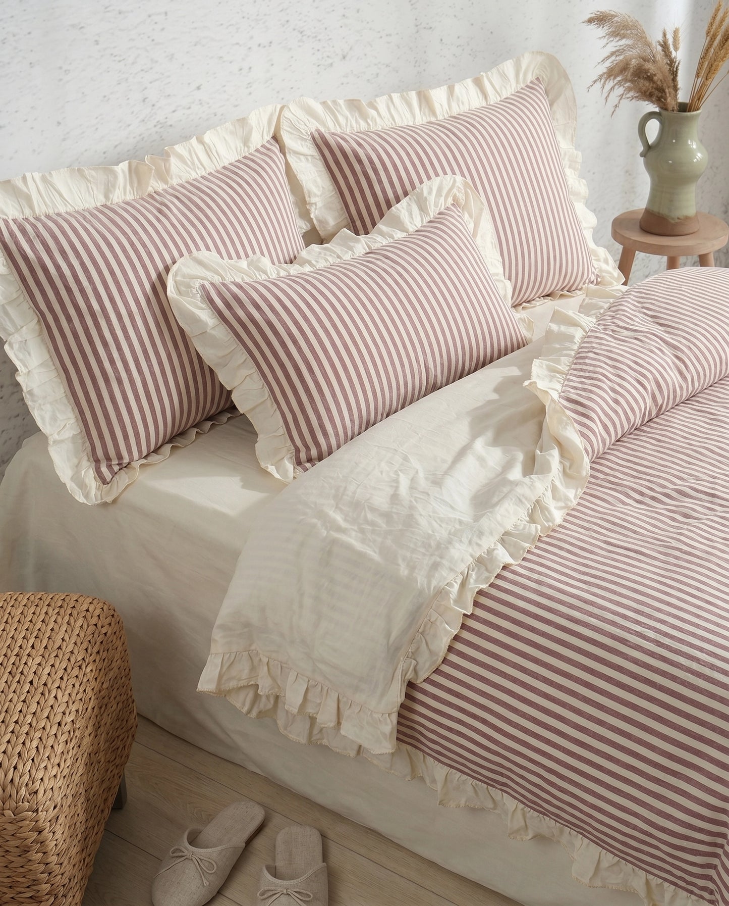 Blush pink striped cotton bedding with ruffle pillow shams and ivory duvet cover styled in a cozy neutral bedroom