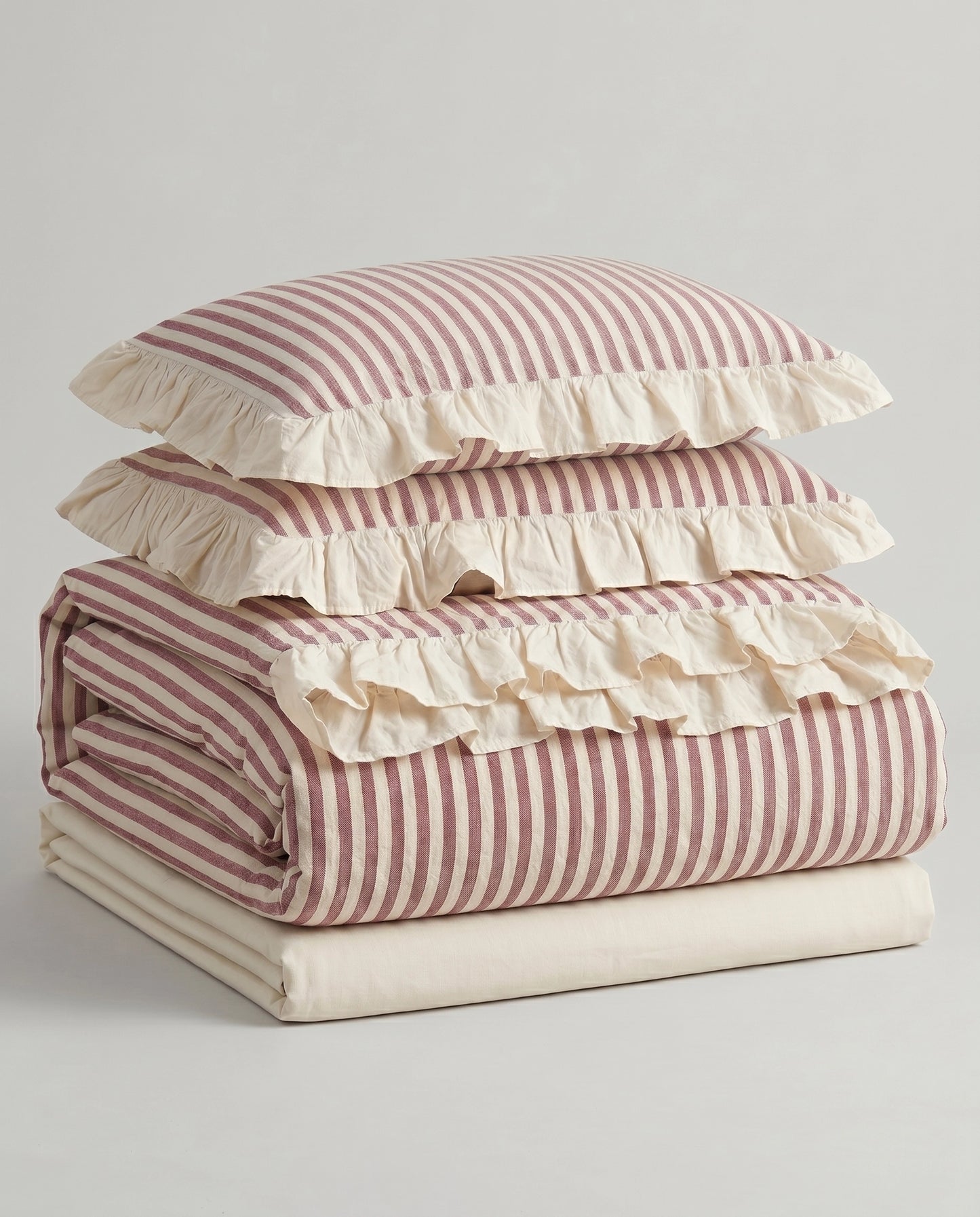 Folded blush pink striped cotton bedding set with ivory ruffle trim and soft vintage inspired duvet cover styling