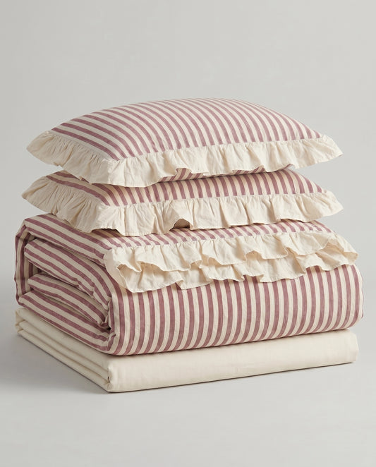 Folded blush pink striped cotton bedding set with ivory ruffle trim and soft vintage inspired duvet cover styling