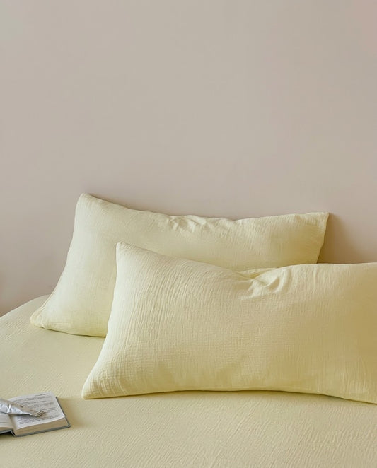 Two Butter muslin cotton double gauze pillowcases on a matching fitted sheet with an open book
