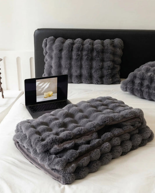 Folded DORMÉ Studio Marshmallow Ultra Plush Blanket in charcoal plush texture displayed on minimalist bed with matching pillows. Black