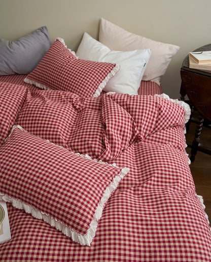 Relaxed unmade bed with a gingham duvet cover and ruffled pillowcases beside white, grey and blush pillows