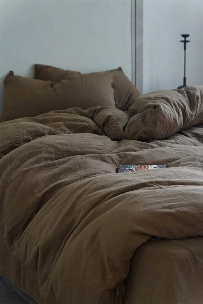 Relaxed unmade bed with Truffle muslin cotton duvet cover, pillowcases and a magazine