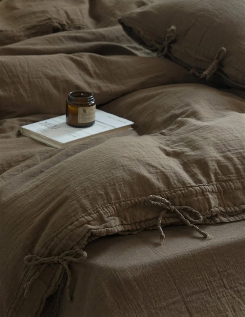 Truffle muslin duvet cover with bow tie closures and an amber candle on a book
