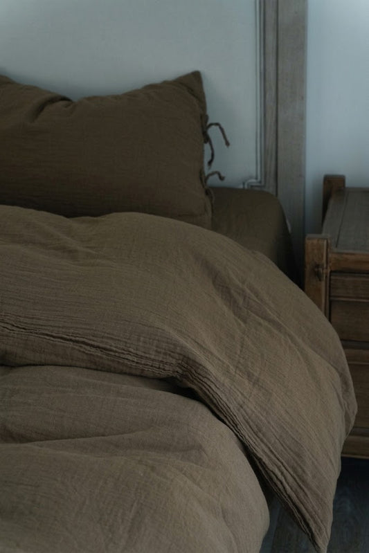 Truffle muslin cotton duvet cover draping beside a wooden nightstand with a tie-closure pillowcase