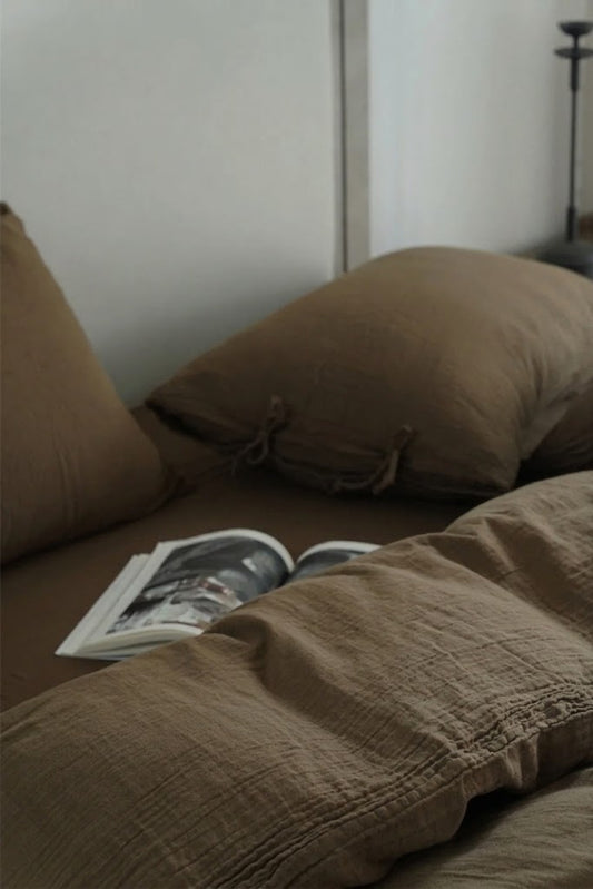 Truffle crinkled muslin pillowcase with side tie closures and an open magazine on a made bed