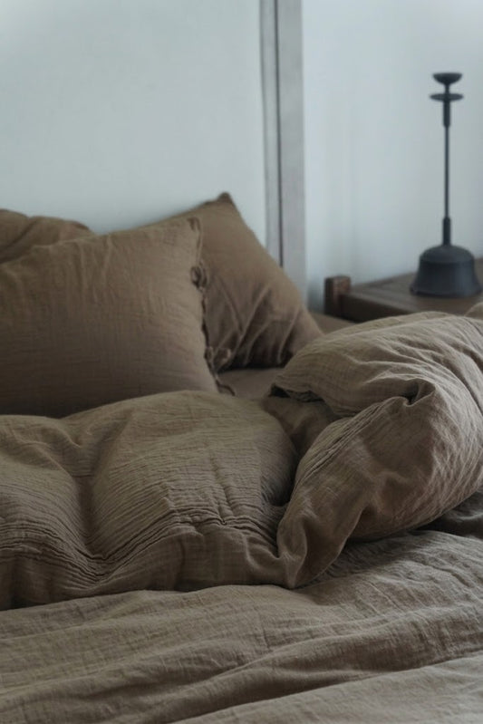 Close-up of crinkled Truffle muslin duvet cover and pillowcases with a black candlestick
