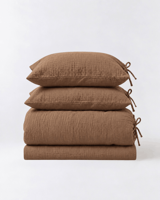 Folded Cinnamon muslin cotton duvet cover set by DORMÉ Studio showing duvet cover, flat sheet, and two tie-closure pillowcases
