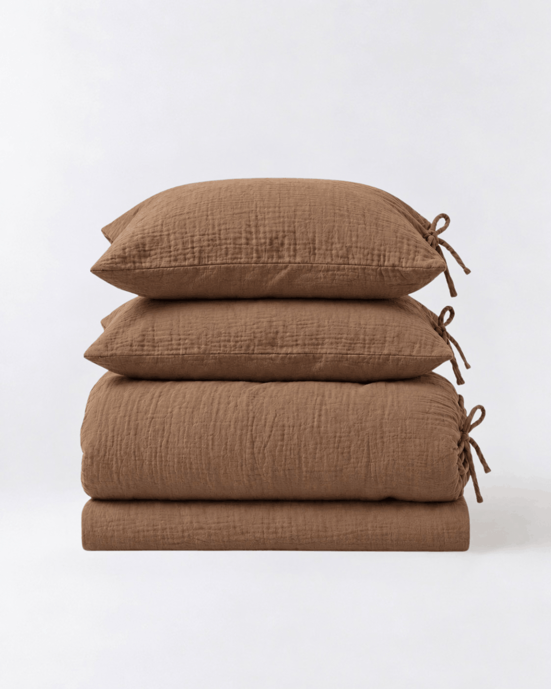 Folded Cinnamon muslin cotton duvet cover set by DORMÉ Studio showing duvet cover, flat sheet, and two tie-closure pillowcases