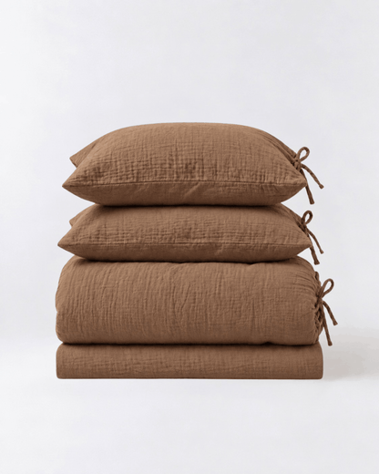 Folded Cinnamon muslin cotton duvet cover set by DORMÉ Studio showing duvet cover, flat sheet, and two tie-closure pillowcases
