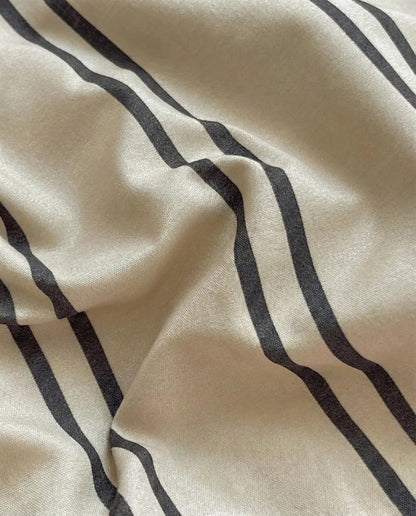 Beige cotton bedding fabric with thin dark stripe pattern showing smooth, breathable texture