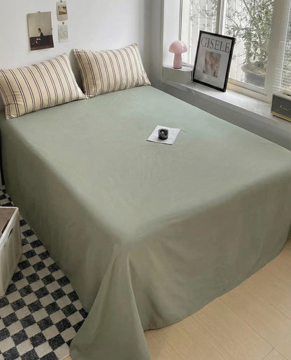 Olive green flat sheet paired with beige striped pillowcases in clean modern bedroom setup