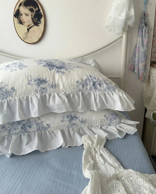 Ruffled floral pillowcases with blue rose pattern styled against ivory bedding