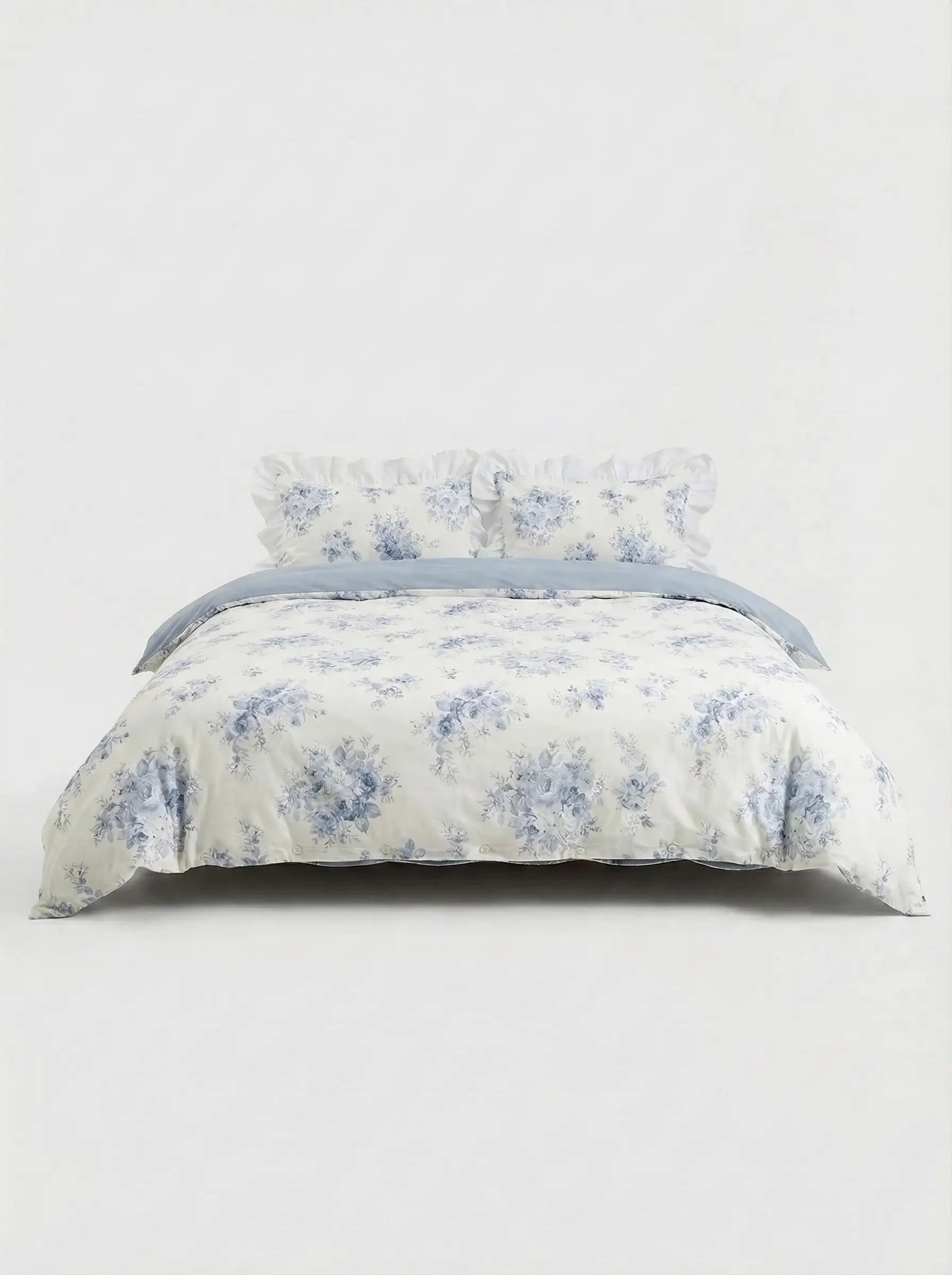 Blue floral ruffled duvet cover set with matching pillow shams styled on bed against clean white studio background