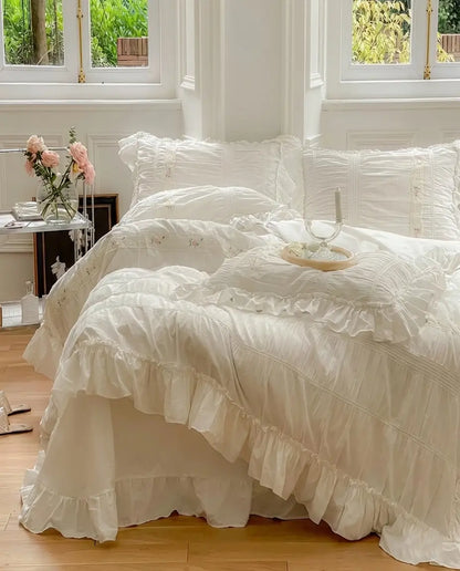 White ruched duvet cover set with ruffle trim and embroidered floral details styled on bed in elegant bedroom
