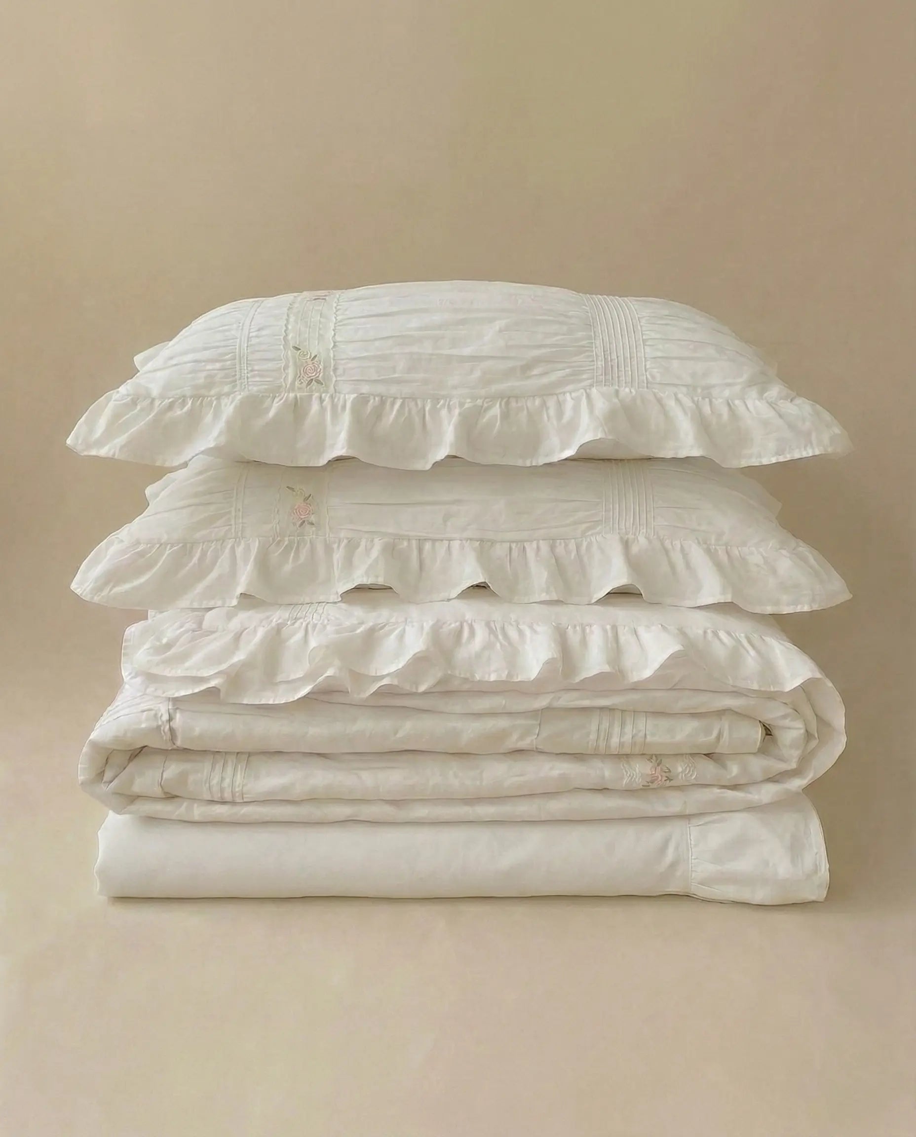 Folded white ruched duvet cover set with matching pillowcases on neutral studio background