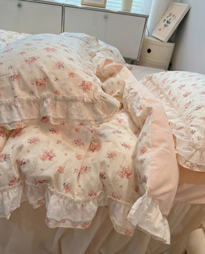 Romantic floral comforter with delicate lace edges styled on pastel pink bed in sunlit cottage bedroom
