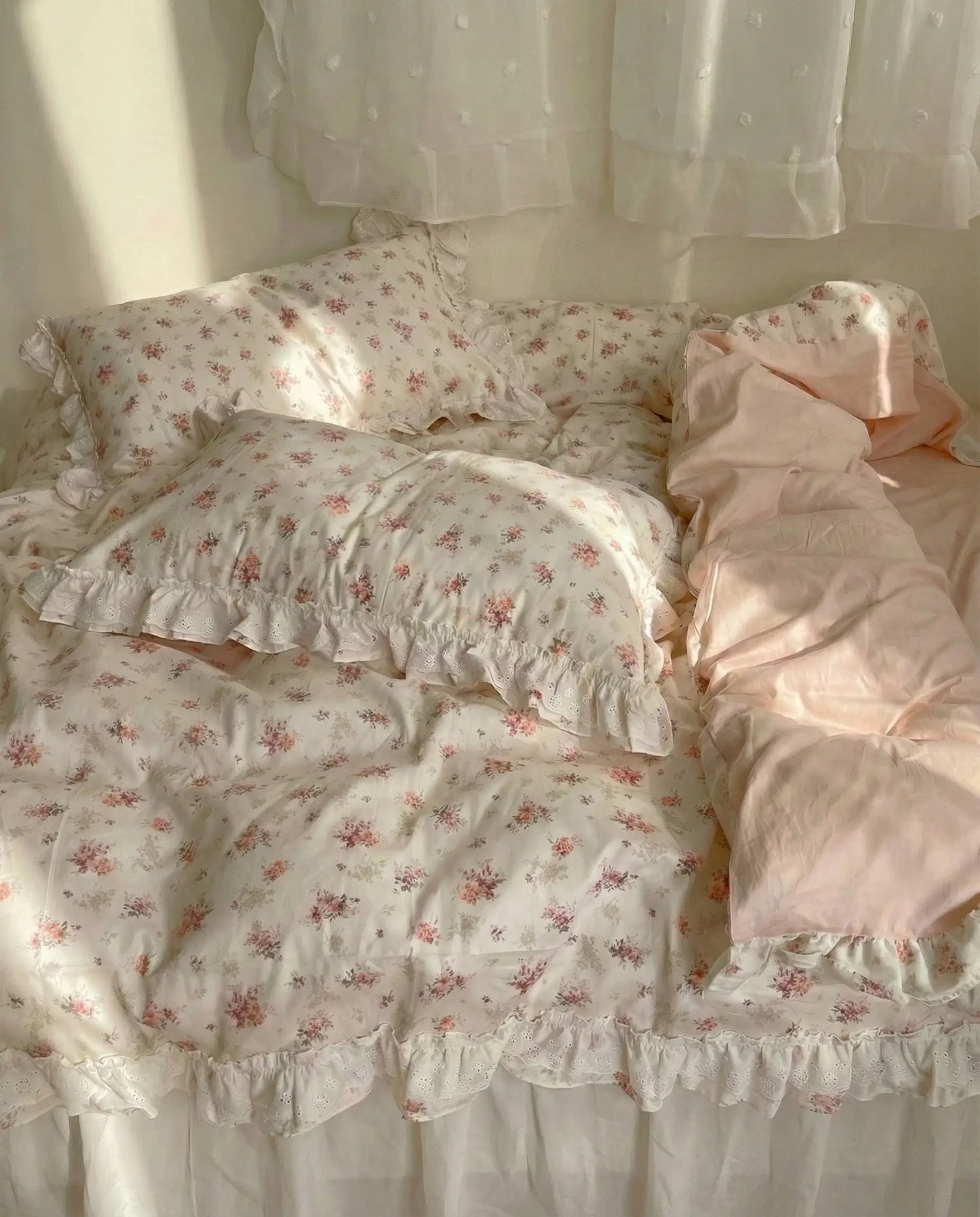 Ivory floral duvet cover with lace ruffle trim and blush pink sheets styled on cozy romantic bed