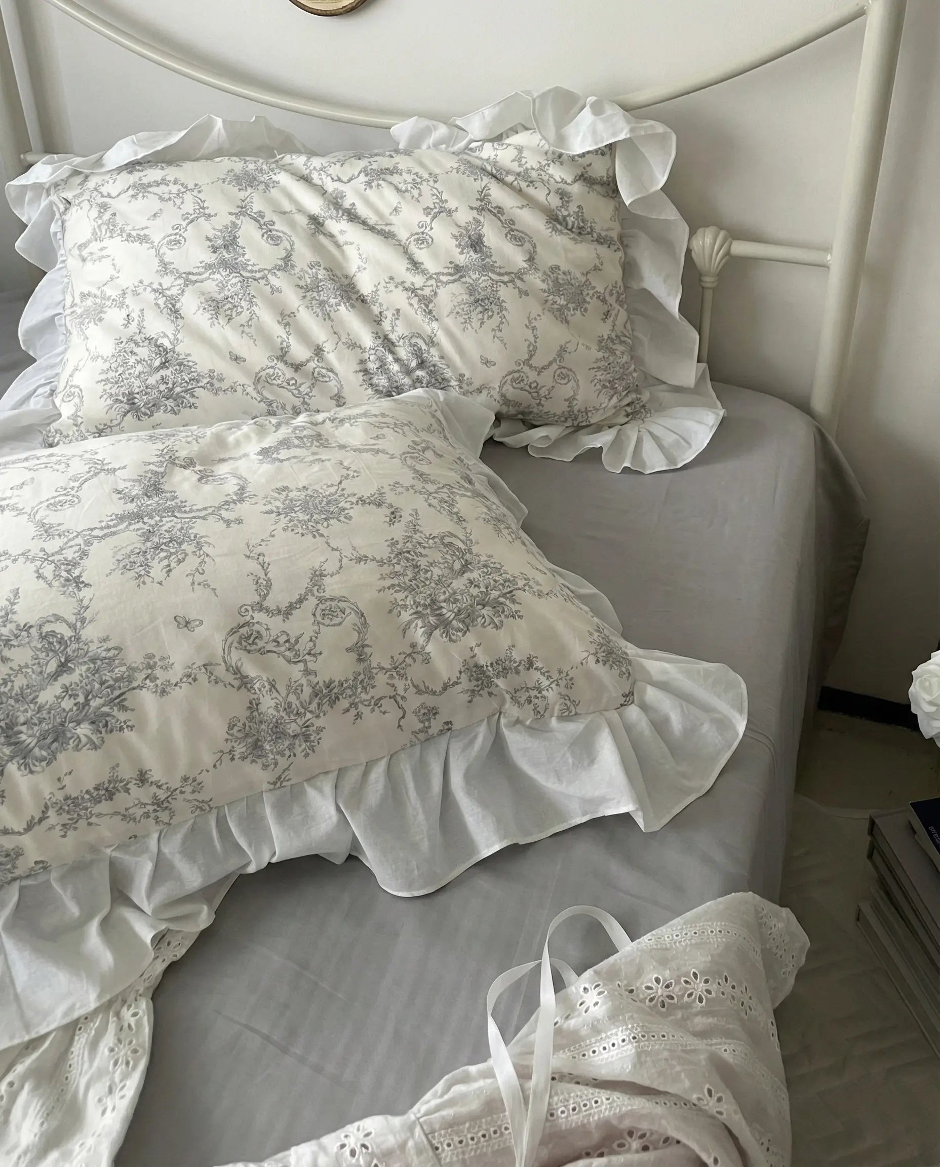 Grey toile floral pillow and duvet with soft ruffled trim layered on a white bed frame, highlighting classic vintage pattern, aesthetic bedding, vintage bedding, floral pillows, white bedding, grey floral, romantic bedroom, cottage bedroom, bedroom decor