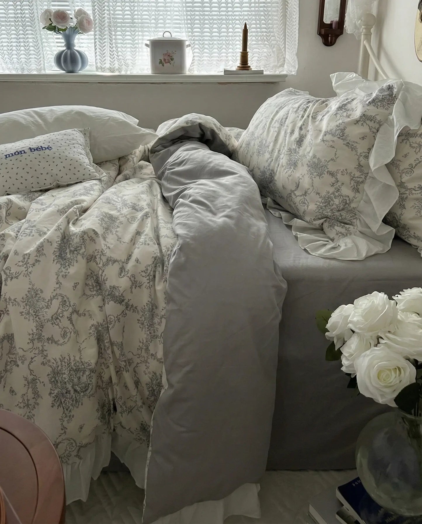 Ivory floral duvet cover draped over bed with gray fitted sheet and ruffled pillowcase, styled beside window with soft natural light and neutral bedroom decor