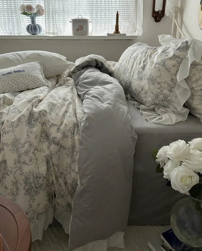Ivory floral duvet cover draped over bed with gray fitted sheet and ruffled pillowcase, styled beside window with soft natural light and neutral bedroom decor