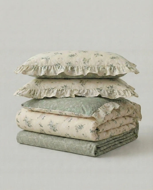 Folded floral bedding set with sage green botanical print and ruffled trim in studio product photo