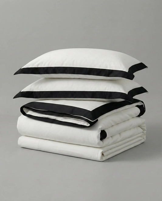 Folded white duvet cover set with black trim and matching pillowcases on neutral studio background