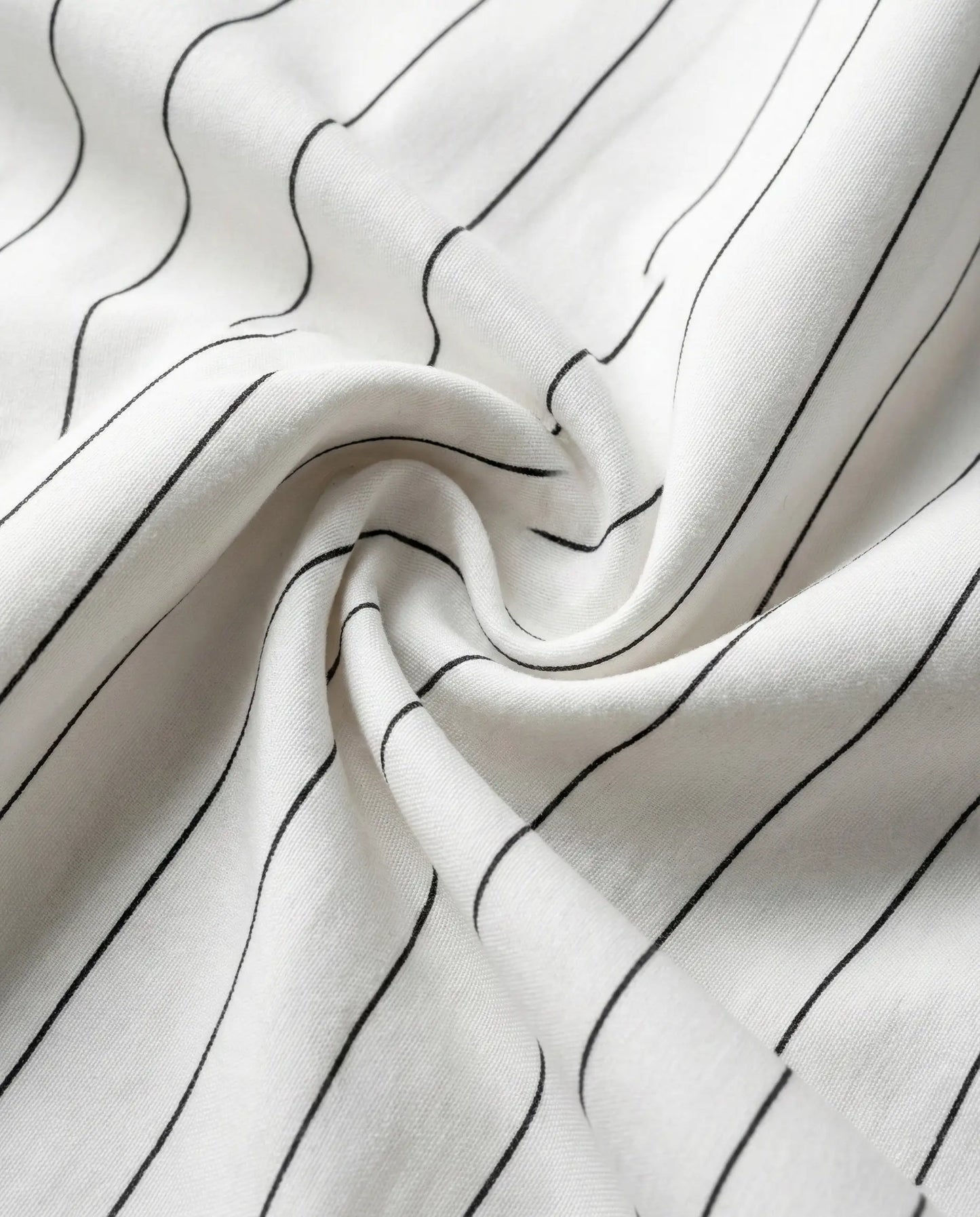 Close-up of white pinstripe bedding fabric showing smooth weave, soft drape, and fine black stripes for a modern minimalist bedroom look.
