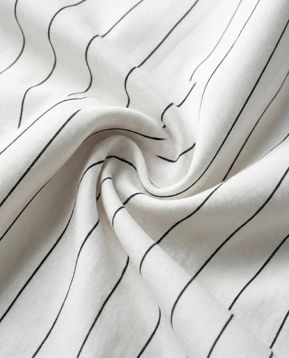 Close-up of white pinstripe bedding fabric showing smooth weave, soft drape, and fine black stripes for a modern minimalist bedroom look.