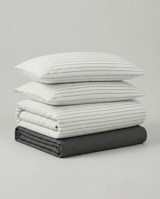 Minimalist striped duvet cover set folded with matching pillowcases and charcoal fitted sheet, featuring thin black pinstripes on soft white fabric.