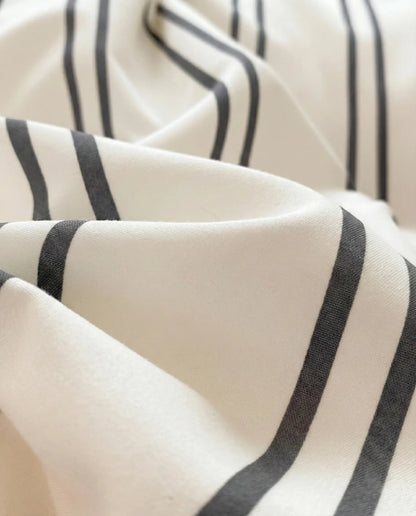 Close-up of silky smooth striped bedding fabric with a lightweight drape, offering a refined look and comfortable feel for everyday sleep.