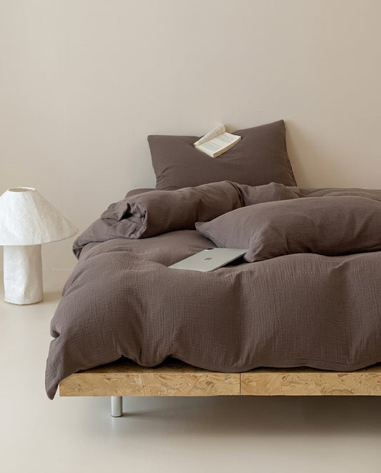 Espresso muslin cotton double gauze duvet cover set on a wooden platform bed beside a paper lamp