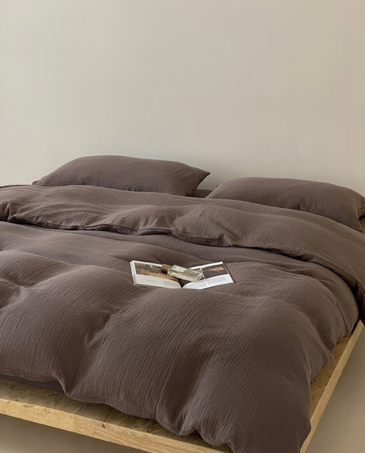 Espresso muslin cotton double gauze duvet cover and pillowcases on a wooden bed with an open magazine