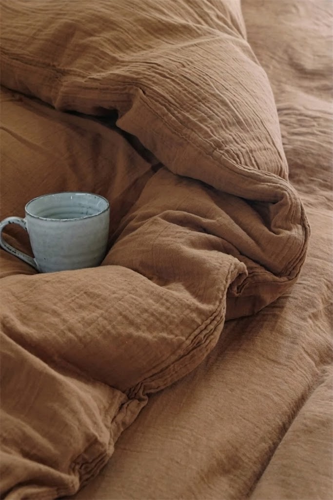 Crinkled Cinnamon muslin cotton duvet cover with a ceramic mug on a relaxed unmade bed