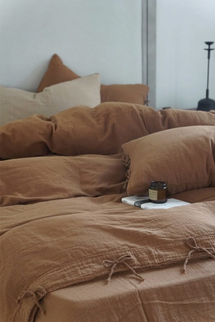 Cinnamon muslin cotton duvet cover with bow tie closures, styled with a neutral accent pillow and an amber candle