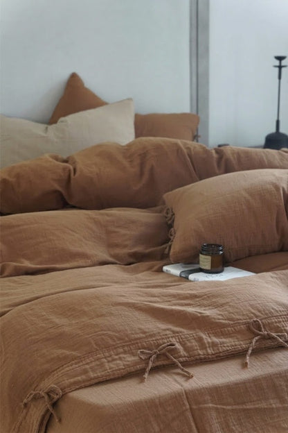 Cinnamon muslin cotton duvet cover with bow tie closures, styled with a neutral accent pillow and an amber candle