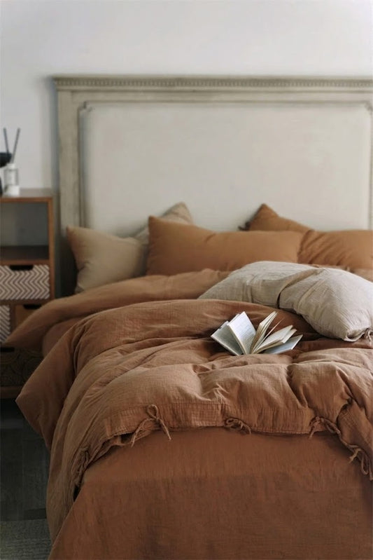 Cinnamon muslin cotton duvet cover and pillowcases against a carved upholstered headboard with an open book