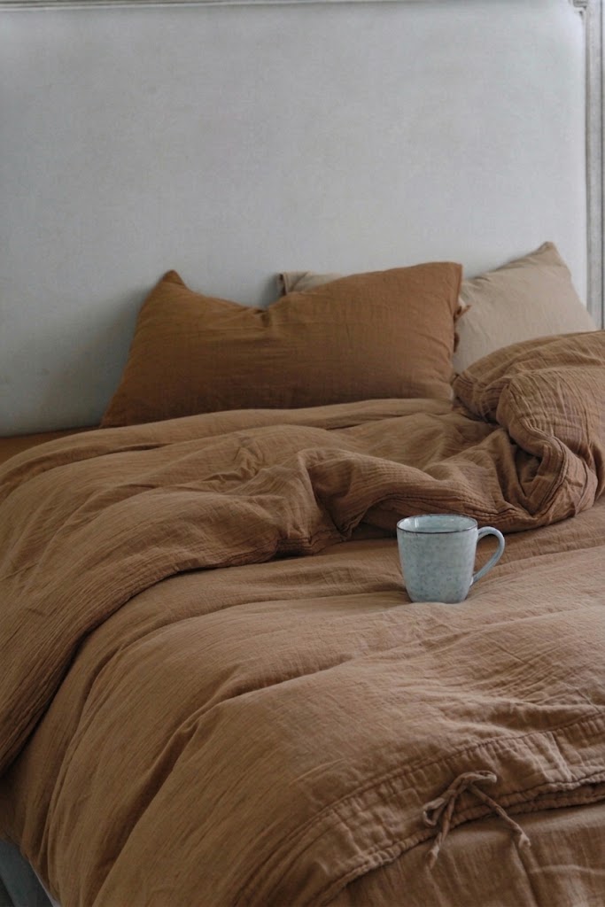Cinnamon muslin duvet cover and pillowcases with a ceramic mug on a relaxed bed against a painted headboard