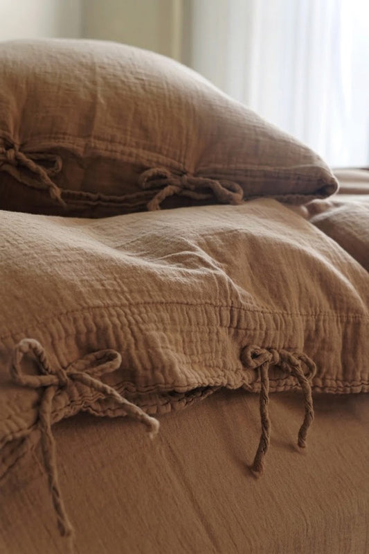 Close-up of Cinnamon muslin cotton pillowcases with bow tie closures in soft window light