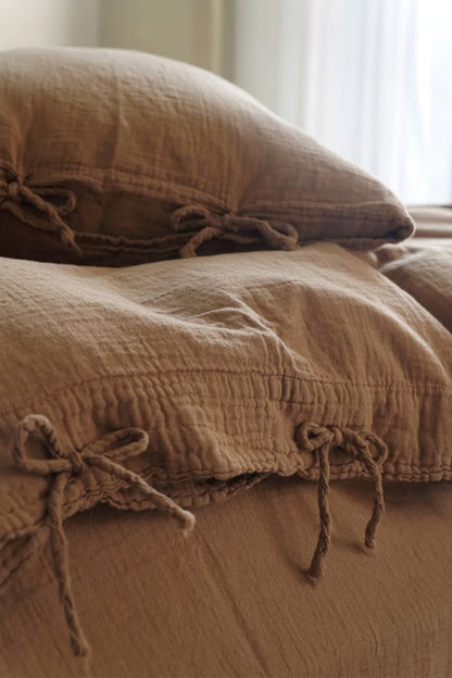 Close-up of Cinnamon muslin cotton pillowcases with bow tie closures in soft window light
