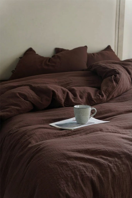 Chocolate Espresso muslin duvet cover set with bow tie closures and a ceramic mug on a relaxed unmade bed