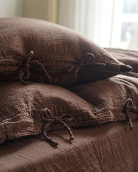 Close-up of chocolate espresso muslin cotton pillowcases with tie closures in soft window light