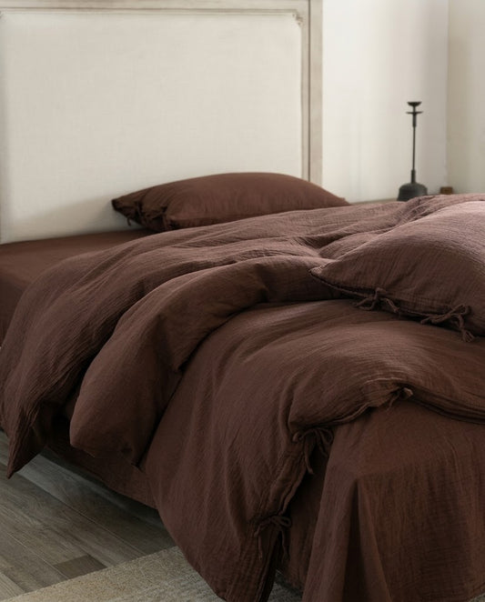 Chocolate espresso muslin duvet cover and flat sheet draping to the floor, with tie closures and a neutral headboard