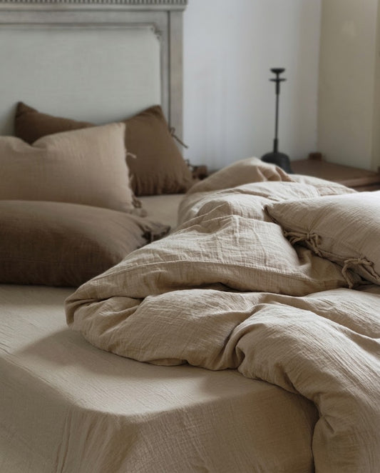 Rumpled Natural Oat muslin cotton duvet cover on a matching sheet, with pillowcases against a painted headboard